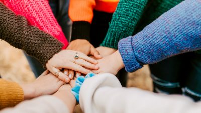 A closeup of hands reaching in from a circle with vibrant colored sweaters.